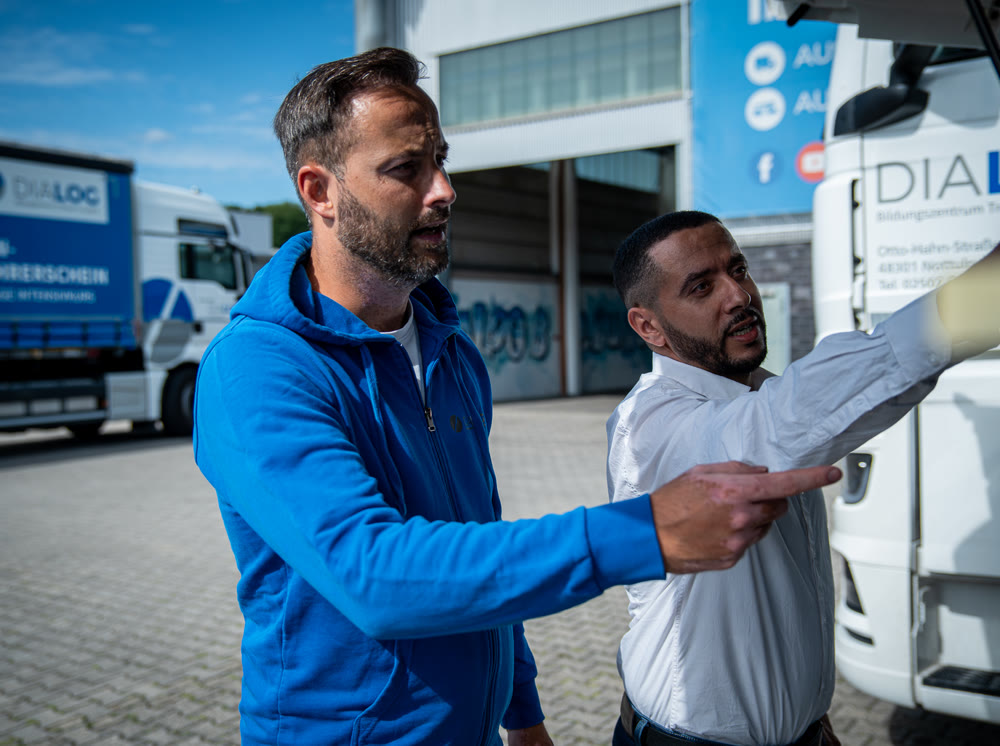 Praxisausbildung bei DIALOG: Ausbilder erklärt einem Fahrer die Spiegeleinstellung am LKW